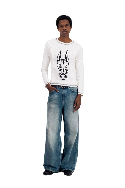Man wearing a white long-sleeve shirt with a black graphic design and blue jeans on a white background